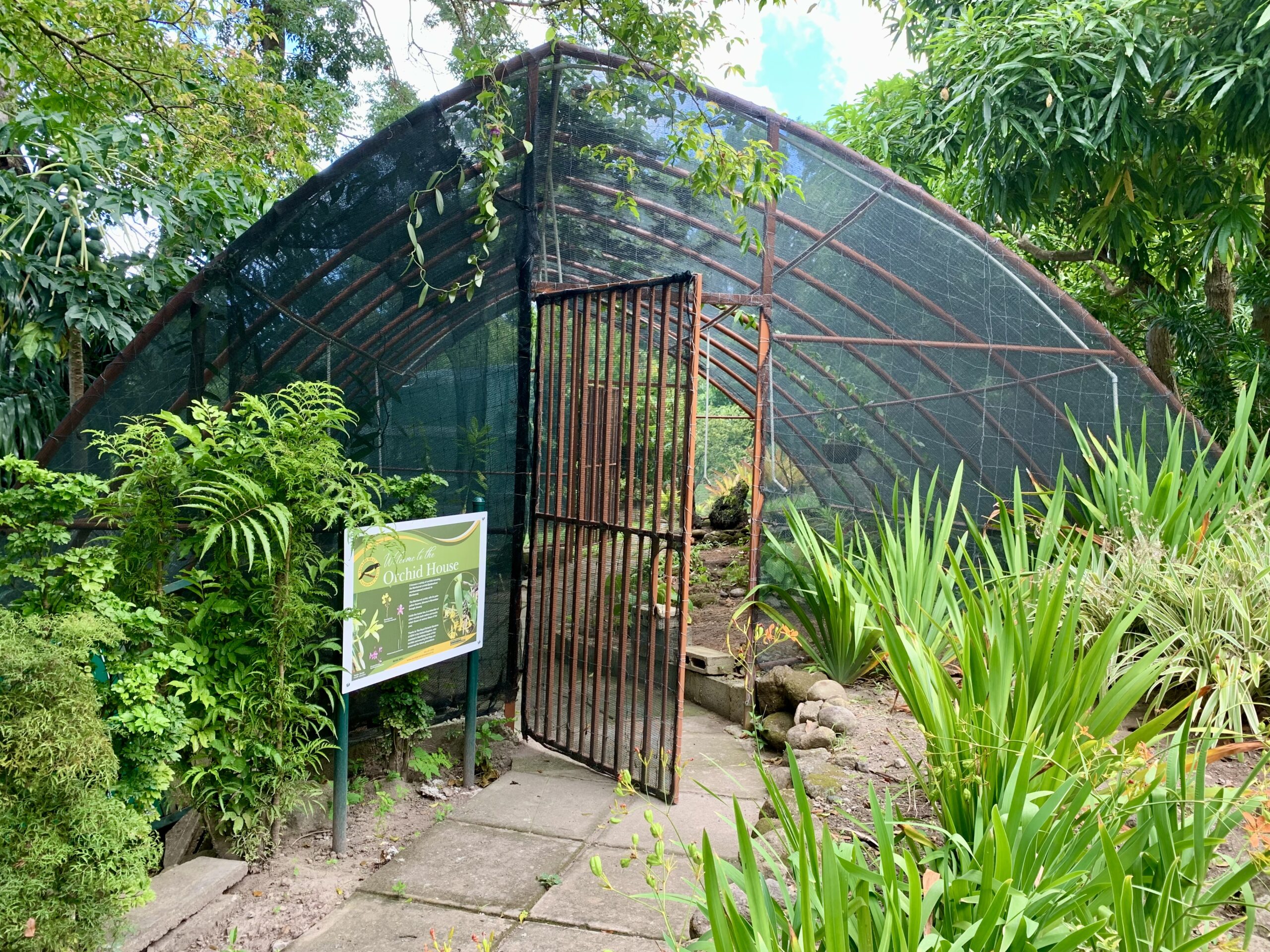 Wide shot of a sign reading "orchid house" with an open red gate leading into a protected garden.