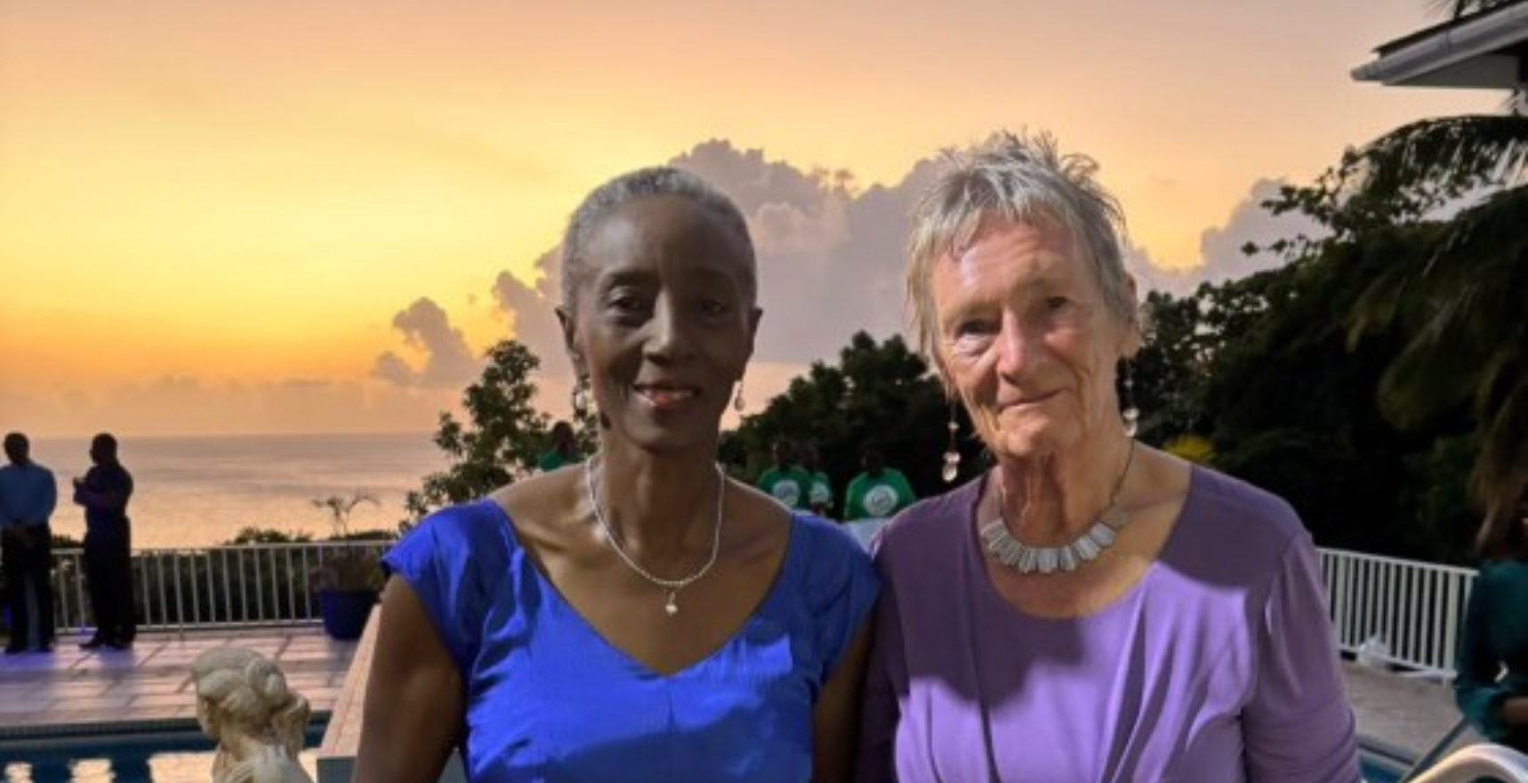 Two women wearing cocktail dresses posing in front of a sunset